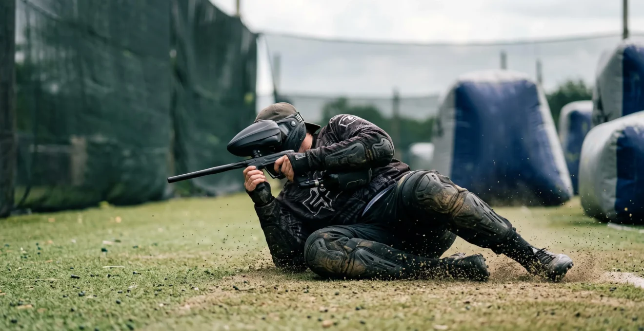 Joueur de paintball en position de glissade portant des genouillères et coudières techniques sur un terrain extérieur