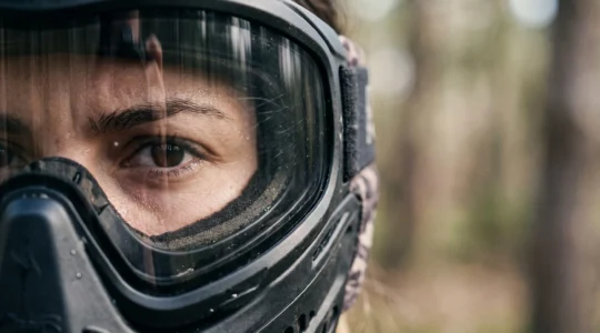 Gros plan sur un joueur de paintball dont le regard reflète la vigilance derrière un écran de masque de protection