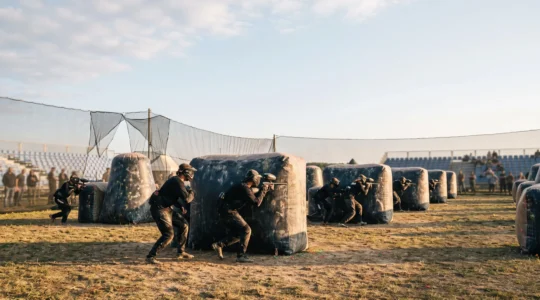 Terrain de compétition de paintball européen avec joueurs en position tactique derrière des bunkers gonflables, symbolisant la hiérarchie des divisions